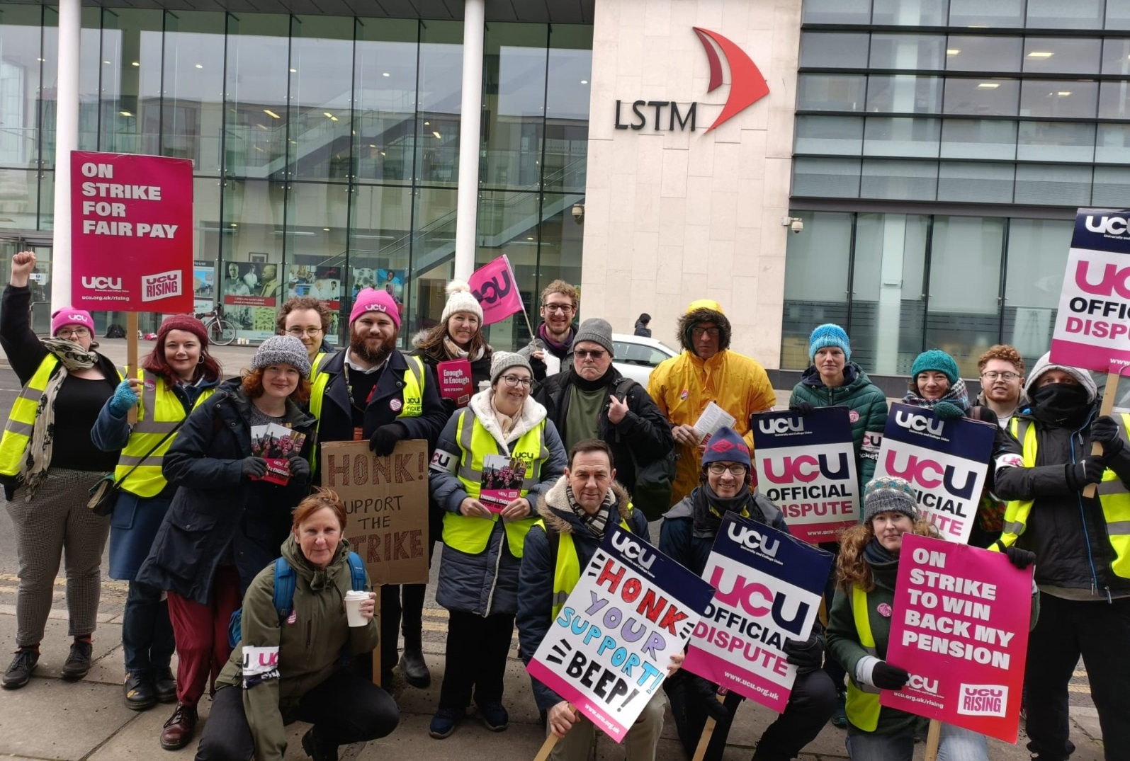 LSTM members picketing outside one of their buildings. They hold placards saying 'on strike to win back my pension', 'on strike for fair pay', and 'Honk your support Beep!'