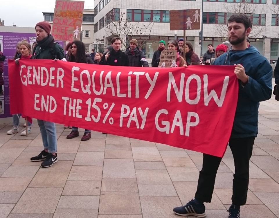 Two striking members of Liverpool UCU hold a banner reading 'gender equality now end the 15% pay gap'. It is a couple of years old!